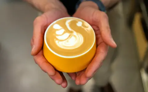 Dłonie trzymają żółtą filiżankę z kawą, na której widnieje wzór łabędzia. Zastanawiasz się, ile kofeiny ma espresso?