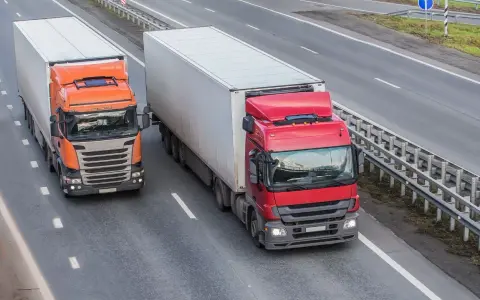 Dwa ciężkie tiry na autostradzie. Czerwony i pomarańczowy, każdy z dużą naczepą. Maksymalny nacisk na oś naczepy to klucz do bezpiecznego transportu.