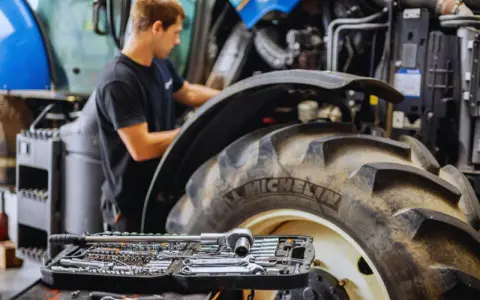 Mechanik sprawdza poziom płynów eksploatacyjnych w traktorze, obok leży zestaw kluczy.