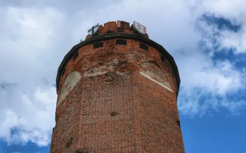 Wieża zamku krzyżackiego w Brodnicy, z cegły, z herbami na szczycie, na tle błękitnego nieba z chmurami.