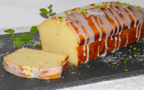 Ein saftiger mallorquinischer Zitronenkuchen mit Zuckerguss und Pistazien, daneben ein angeschnittenes Stück.
