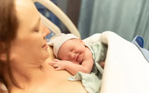 Noworodek śpi na piersi mamy, przygotowując się do karmienia. To piękny początek laktacji i więzi.