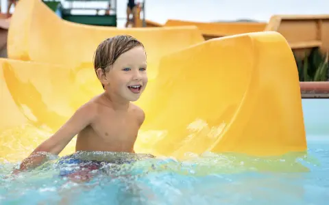 Ein Junge mit blauen Augen lacht fröhlich im Wasser der Wasserrutsche im Heidebad Torgelow.