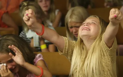 Junge Mädchen erleben emotionale Momente bei einer evangelistischen Religionsveranstaltung, eine jubelt, die andere weint.