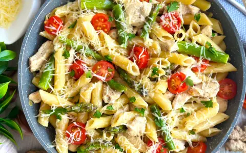 Penne z kurczakiem, szparagami i pomidorkami koktajlowymi, posypane parmezanem. Pyszne danie, które zachwyci każdego smakosza.