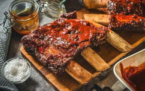 Saftige Rippchen mit BBQ-Sauce, perfekt für Ihre nächsten Grill Rezepte. Dazu grobes Salz und eine Schüssel Sauce.