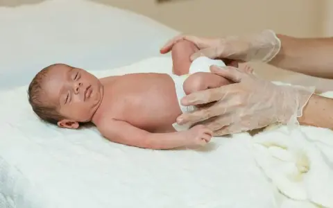 Delikatne badanie niemowlaka, ocena symetrii kończyn. Dłoń w rękawiczce delikatnie dotyka nóżek dziecka.