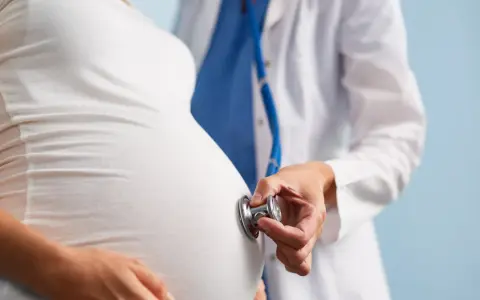 Lekarz osłuchuje brzuch ciężarnej kobiety stetoskopem. Dbałość o zdrowie w ciąży to podstawa.