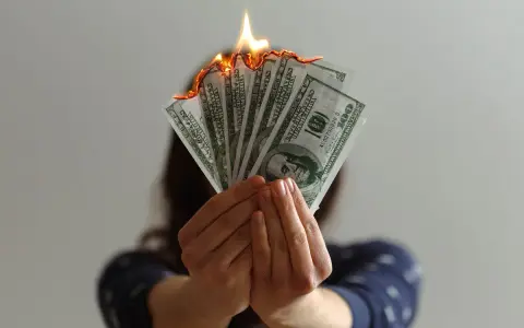 Hands hold burning US dollar bills, a visual metaphor for a use it or lose it budget.