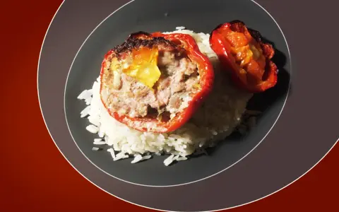 Poivrons rouges farcis à la viande, servis sur un lit de riz blanc. Une sauce légère accompagne ce plat, rappelant les saveurs des tomates farcies.