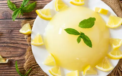 Delizioso gelo di limone su piatto bianco, decorato con spicchi di limone fresco e foglie di menta.