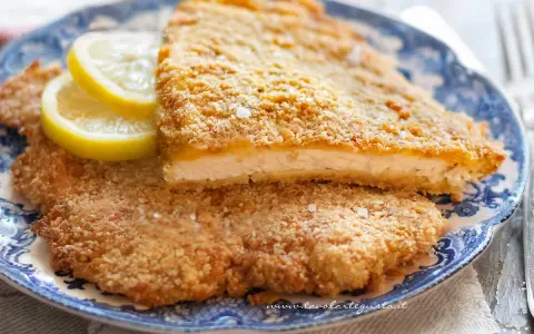 Due cotolette al forno dorate e croccanti, servite su un piatto blu e bianco con spicchi di limone.