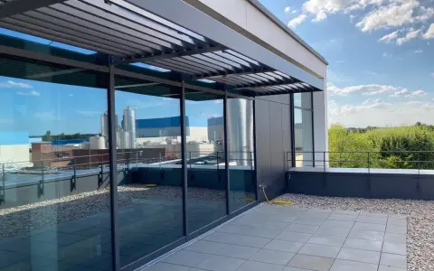 Moderne Dachterrasse mit Glasfront und Lamellendach. Ein gelber Schlauch liegt bereit, um das Flachdach anzuheben und zu pflegen.