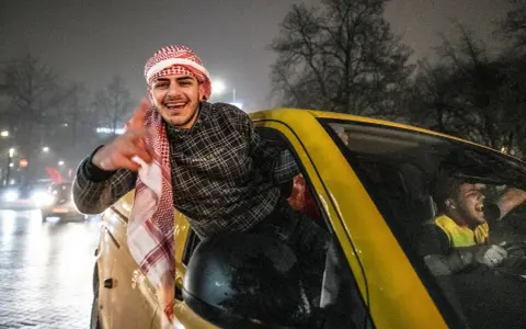 Jonge Marokkaanse Nederlanders vieren feest in een gele auto, met een van hen die uit het raam hangt en lachend zwaait.