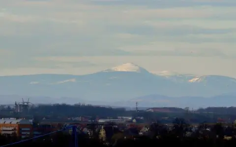 Widok na Śnieżkę i Karkonosze z Wrocławia. Widać ośnieżone szczyty górskie na tle błękitnego nieba.