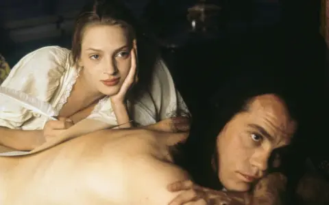 Coppia in un momento intimo, evocativo di scene da film erotici. Lei scrive con una penna d'oca, lui la guarda intensamente.