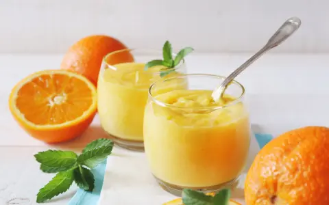 Dwa szklanki orzeźwiającego, gęstego **orange curd** z miętą i świeżymi pomarańczami.