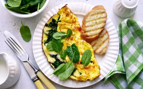Pyszny omlet ze szpinakiem, podany z grzankami i świeżymi liśćmi szpinaku. Idealne śniadanie!
