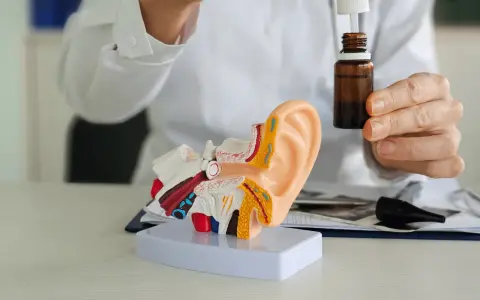 Lekarz pokazuje model ucha i krople, które mogą być antybiotykiem na zapalenie ucha.