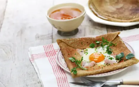 Crêpe de sarrasin garnie d'un œuf au plat, de jambon et d'herbes fraîches, servie avec une compote.