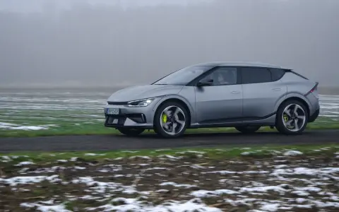 Srebrna Kia EV6 jedzie po drodze, otoczona polami z resztkami śniegu.