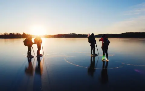Silhuetter av skridskoåkare med stavar och ryggsäckar på en spegelblank is vid solnedgången. En magisk upplevelse av skridskoåkning i Stockholm.