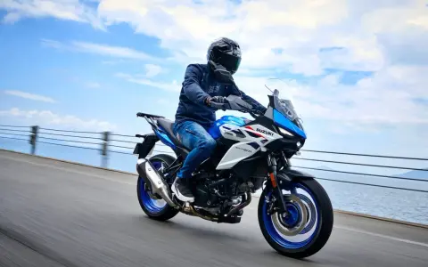 Motocyklista na niebiesko-białym Suzuki SV650X, idealnym motocyklu do 35kW, jedzie wzdłuż wybrzeża.