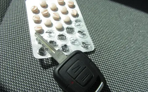Tabletten und Autoschlüssel liegen nebeneinander. Tilidin autofahren ist gefährlich und illegal.