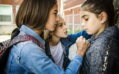 Drei Mädchen stehen eng beieinander. Ein Mädchen wirkt bedrängt, was auf Mobbing in der Grundschule hindeutet.