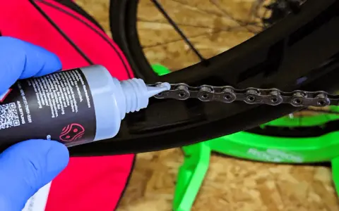 Blaue Handschuhe tragen, um die Fahrradkette wachsen zu lassen. Ein Tropfen Öl fällt auf die Kettenglieder.