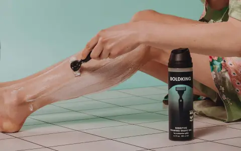 Persona depilándose las piernas con cuchilla y espuma de afeitar.