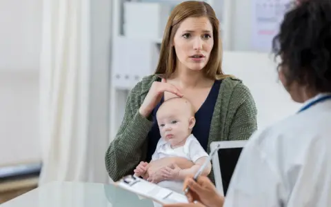Zaniepokojona mama z niemowlęciem na rękach rozmawia z lekarzem. Zastanawia się nad chwilowym zawieszaniem się dziecka.
