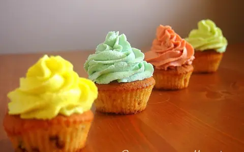 Cztery kolorowe muffiny z kremem: żółtym, miętowym, łososiowym i jasnozielonym.