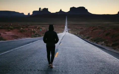 Człowiek idzie pustą drogą w Monument Valley, pogrążony w mysleniu tunelowym, z widokiem na skalne formacje w oddali.