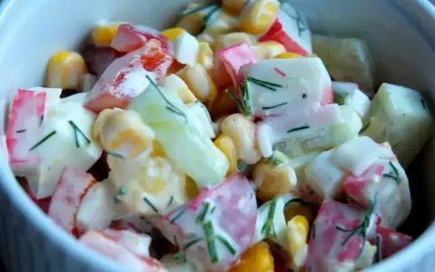 Pyszna sałatka z surimi, kukurydzy, ogórka i jajka, polana kremowym sosem z koperkiem.