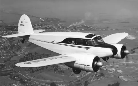 Ein weißes, zweimotoriges hochdecker flugzeug fliegt über eine Stadt und Industrieanlagen.