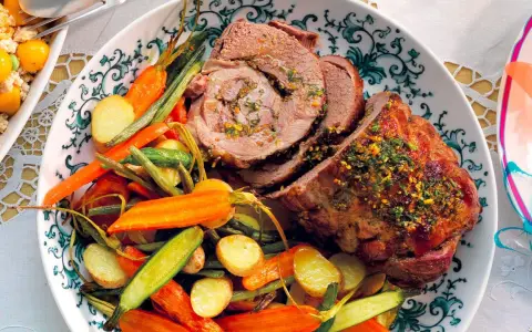 Agnello al forno succulento, affettato e servito con patate novelle, carote e fagiolini croccanti su un piatto decorato.