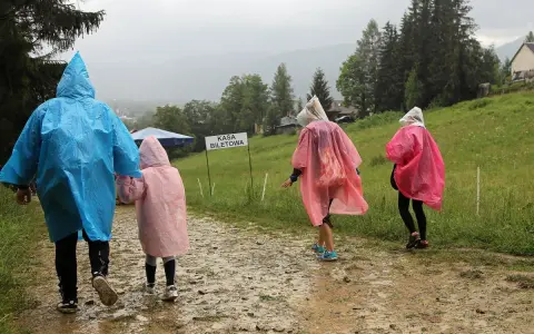 Deszcz w Zakopanem? Nic nie szkodzi! Rodzina w kolorowych pelerynach idzie ścieżką do kasy biletowej, ciesząc się widokami.