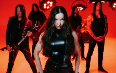 Wokalistka zespołu Arch Enemy w czarnym, błyszczącym stroju, z gitarzystami w tle, na tle czerwonych świateł.