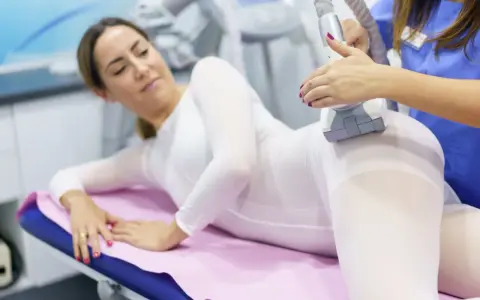 Kobieta w białym kombinezonie poddaje się zabiegowi endermologii. Czy to lepsze niż lipolaser czy liposukcja kawitacyjna?