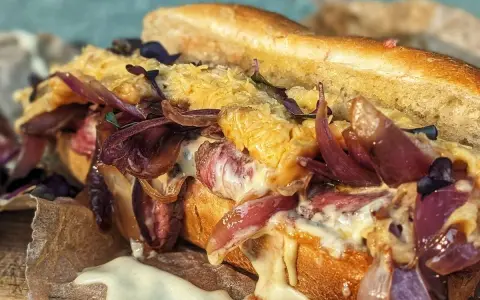 Ein saftiger Philly Cheesesteak-Sandwich mit geschmolzenem Käse, karamellisierten roten Zwiebeln und zartem Rindfleisch auf einem Baguette.