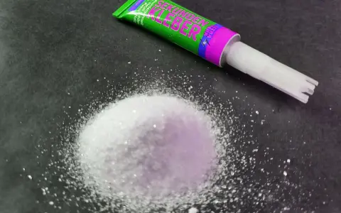 A pile of white granular material sits next to a tube of "Sekunden Kleber" super glue, ready for a quick fix.