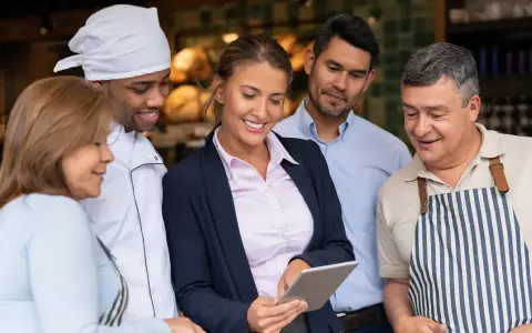 Equipo revisando tablet para la gestión de restaurantes. Chef, gerentes y personal colaboran.