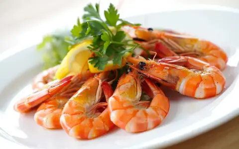 Gambas al ajillo receta: jugosas gambas cocinadas con ajo y perejil, servidas con limón y lechuga en un plato blanco.