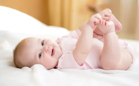 Ein lächelndes Baby von 8 Wochen liegt auf dem Rücken und spielt mit seinen Füßen.