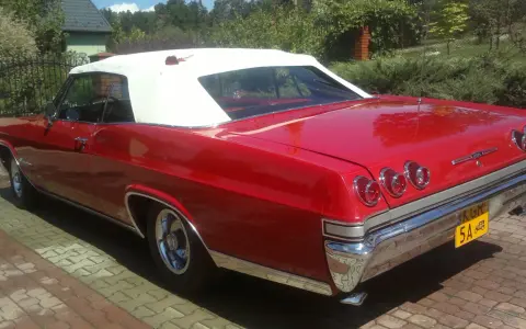 Czerwona kabrioletowa Chevy Impala z białym dachem, zaparkowana na podjeździe z kostki brukowej.