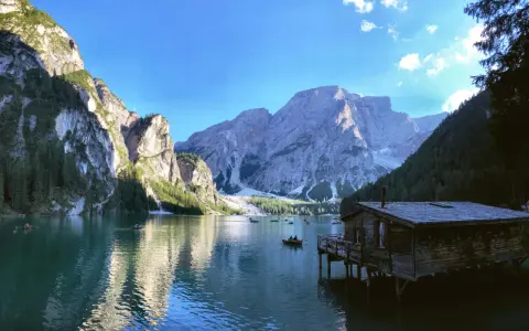 Malownicze jezioro w Dolomitach, z górami w tle i drewnianym domkiem na wodzie. Idealne miejsce na camping i podziwianie natury.