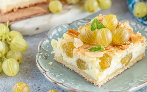 Ein Stück von die besten stachelbeerkuchen, garniert mit frischen Stachelbeeren und Mandelsplittern, auf einem zartblauen Teller.