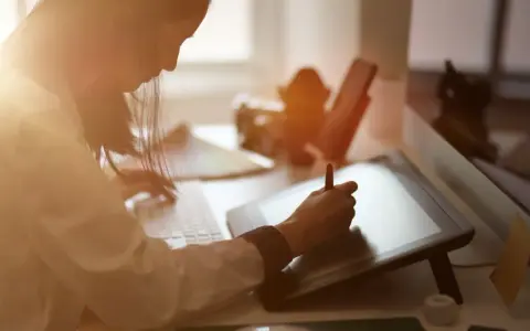 Kobieta tworzy grafikę komputerową, pracując przy tablecie graficznym i klawiaturze.
