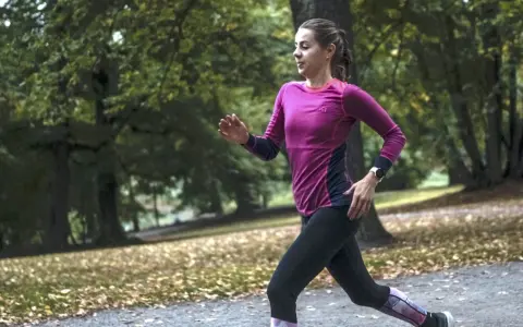 Kvinna springer i parken, fokuserad på att förbättra sin löpning. Frågan "hur blir man snabbare" besvaras med träning.